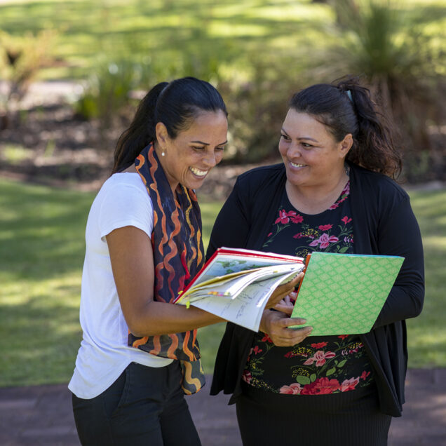 Young aboriginal student talking to her tutor outdoors in the sun in Australia.