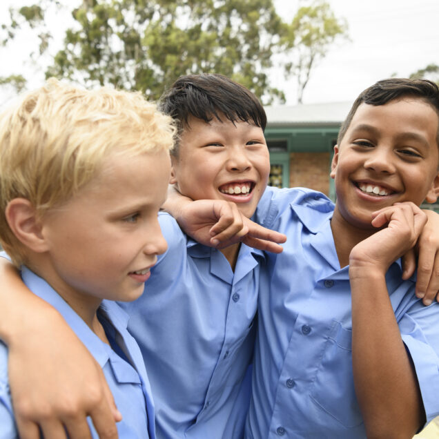 Candid portrait of three boys in school playground with arms around each other